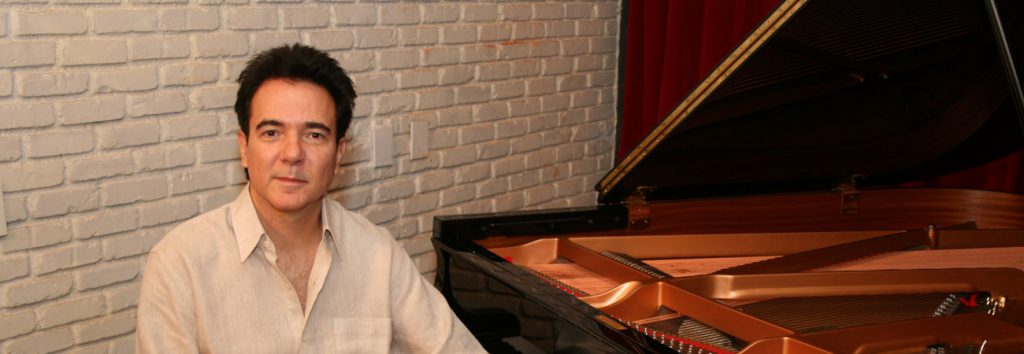 Luciano Alves no estúdio ao lado do piano de cauda.